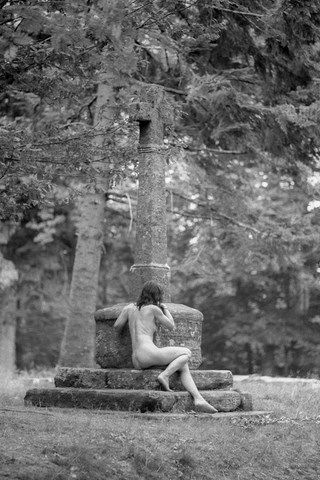 Femme nue au pied d'un croix en forêt