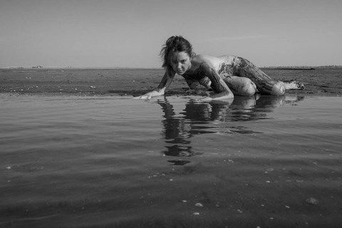 Femme nue, recouverte de sable au bord de la plage