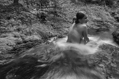 Femme nue, assise dans un ruisseau de montagne
