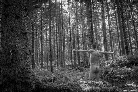 Homme nu à genoux, les bras en croix entre les arbres du massif du Fossard